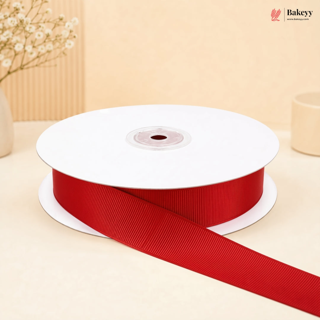 A spool of red grosgrain ribbon with a long tail unwinding, set against a warm beige background with decorative dried flowers.