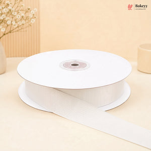 A spool of white grosgrain ribbon with one end unspooled, set against a warm beige background with decorative dried flowers.