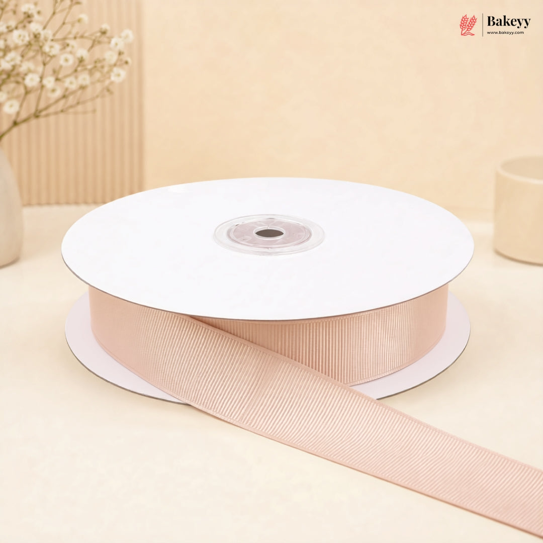 A spool of light pink grosgrain ribbon with a matching ribbon trail draped across the front, set against a warm beige background with soft decorative props.
