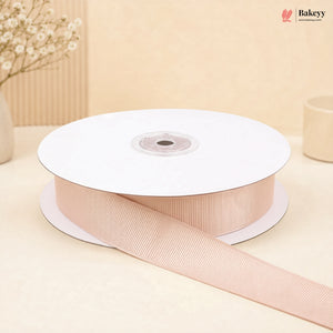 A spool of light pink grosgrain ribbon with a matching ribbon trail draped across the front, set against a warm beige background with soft decorative props.