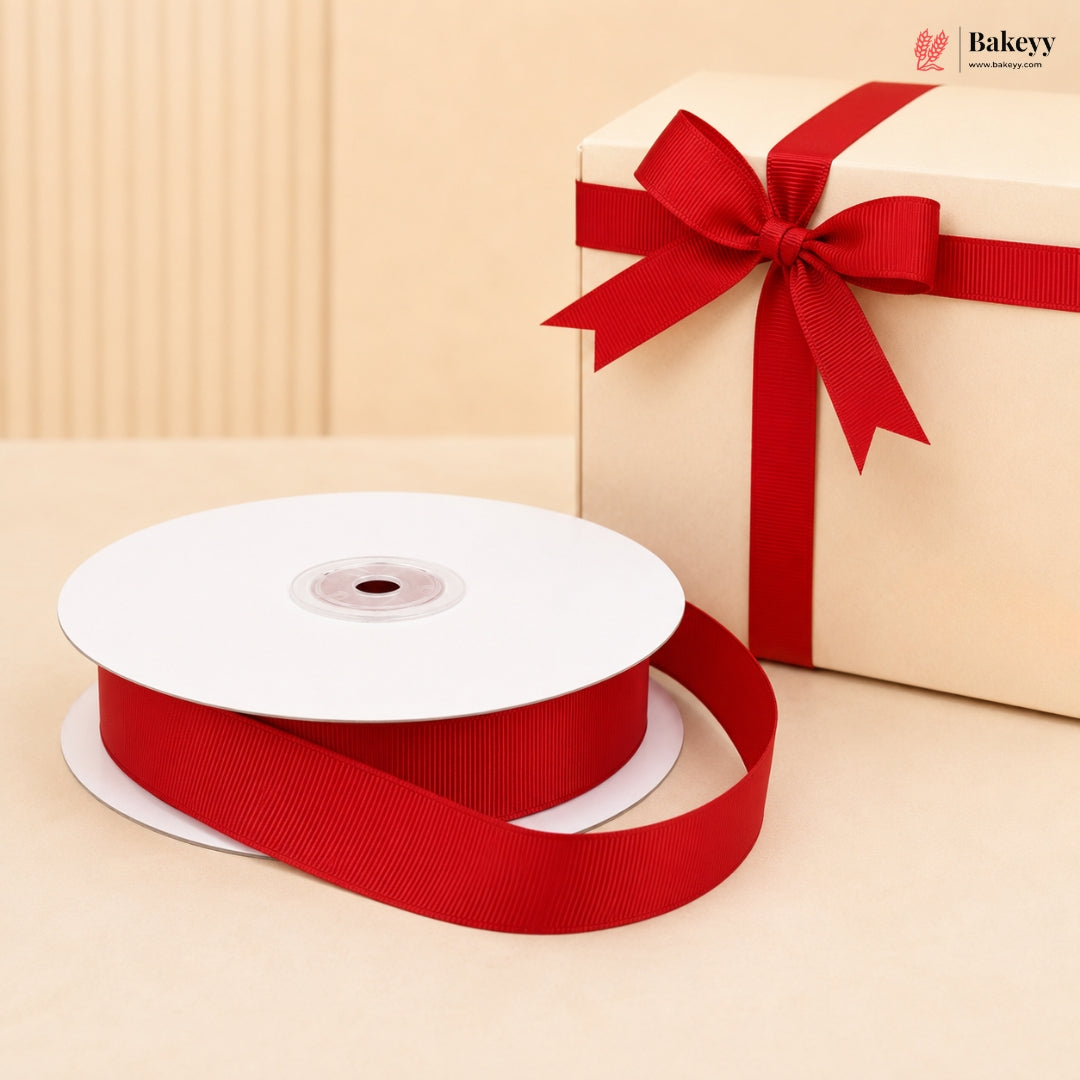 A spool of red grosgrain ribbon with a matching red gift box tied in a bow, set against a warm beige background. The Bakeyy logo is visible in the top right corner.