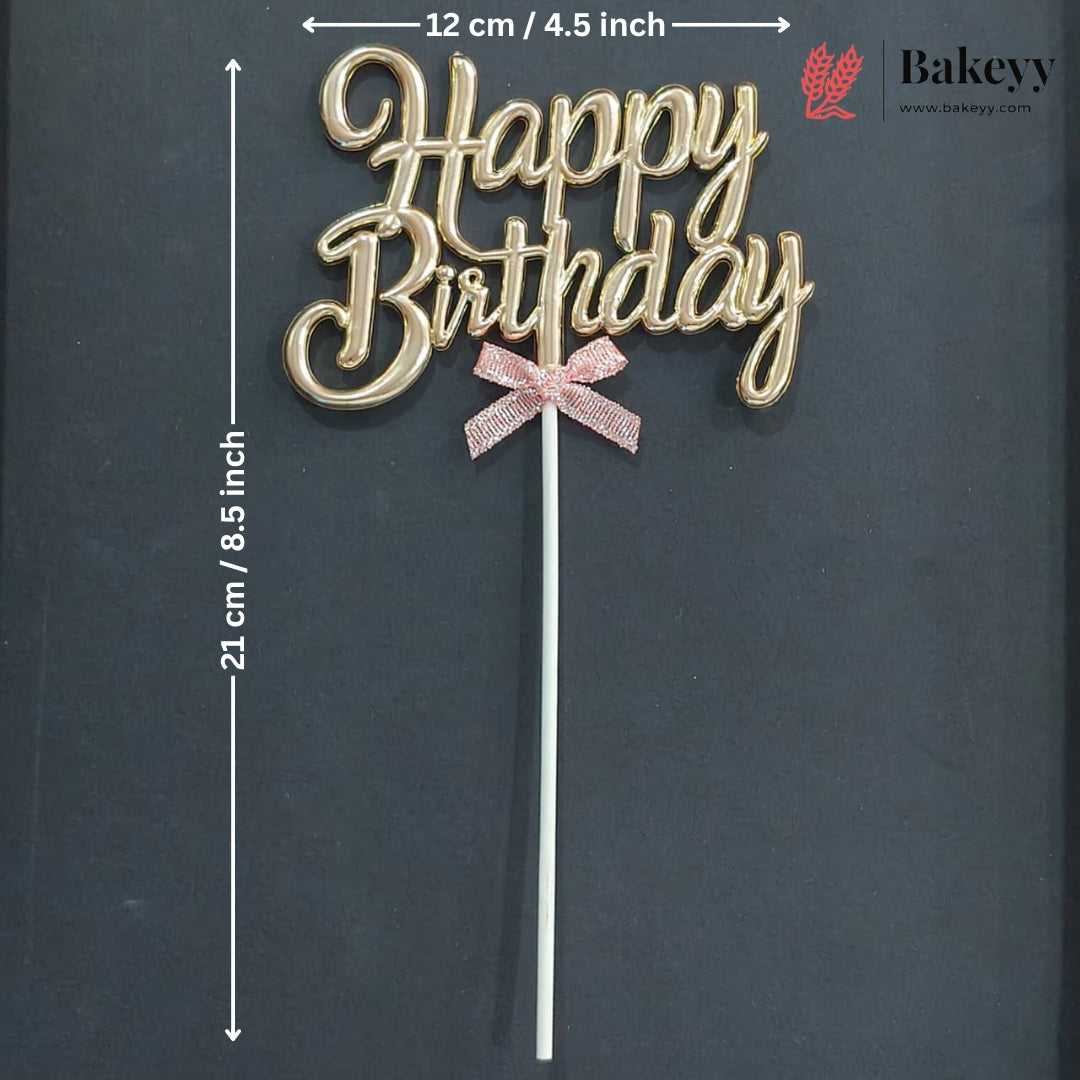 Gold cursive 'Happy Birthday' cake topper with a pink glitter bow on a white stick, shown on a dark background with printed dimensions and a Bakeey logo.