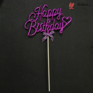 A purple glittery 'Happy Birthday' cake topper with a small bow on a stick, set against a dark background. A Bakeyy logo is visible in the top right corner.