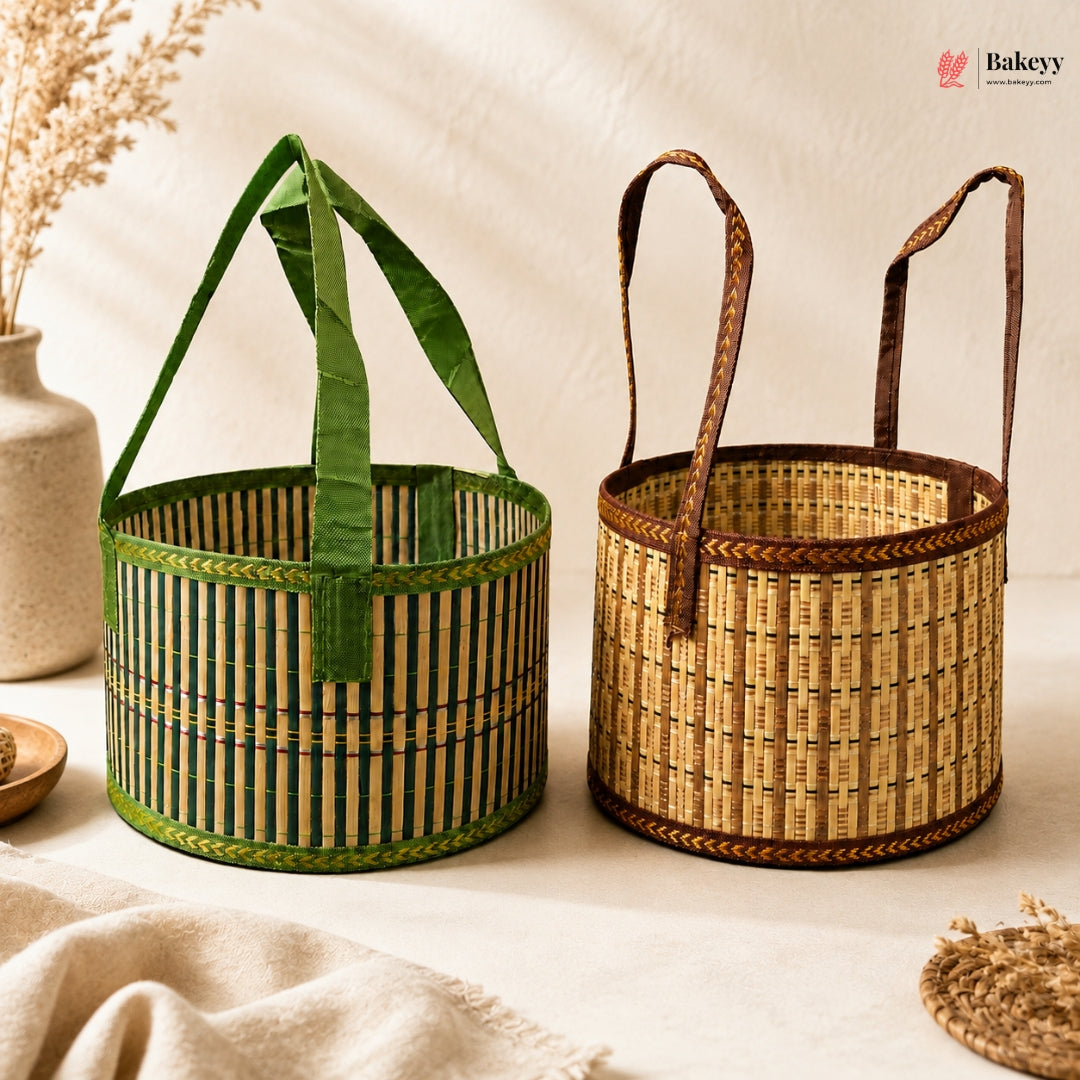 Two woven bamboo baskets with fabric handles, one green and one natural tan, displayed on a neutral cream surface with a beige ceramic vase in the background.