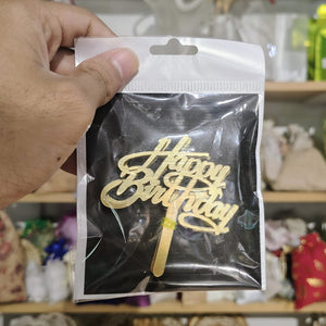 Gold 'Happy Birthday' cake topper in clear packaging held by a hand.
