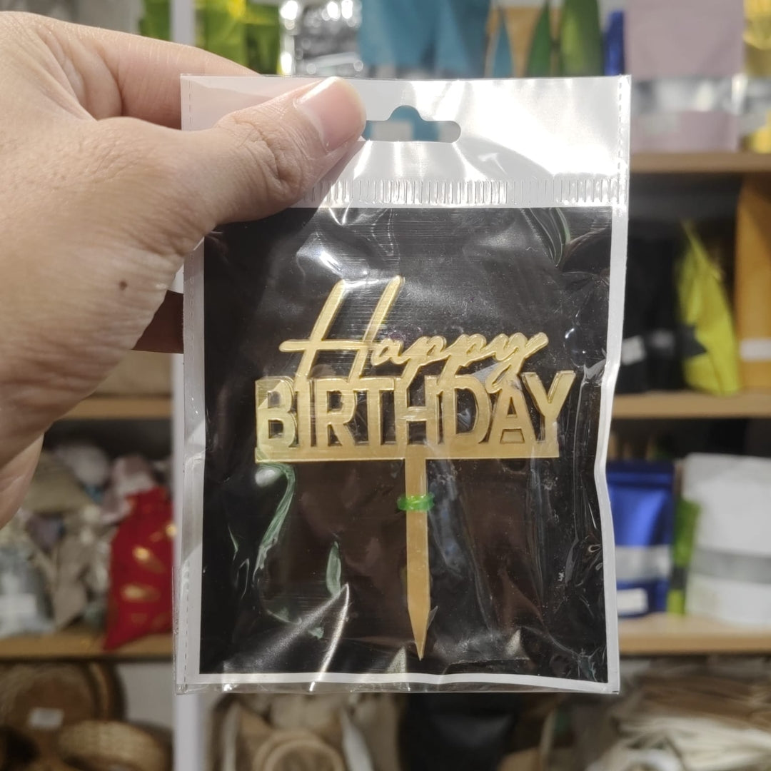 Hand holding a clear plastic bag with 'Happy Birthday' text in gold.
