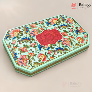 An octagonal decorative gift box with a light mint green base, covered in a colorful floral pattern with pink, red, blue, and yellow flowers, and a central red mandala design on the lid. The box is shown at an angle on a neutral beige background with Bakeyy branding in the corners.