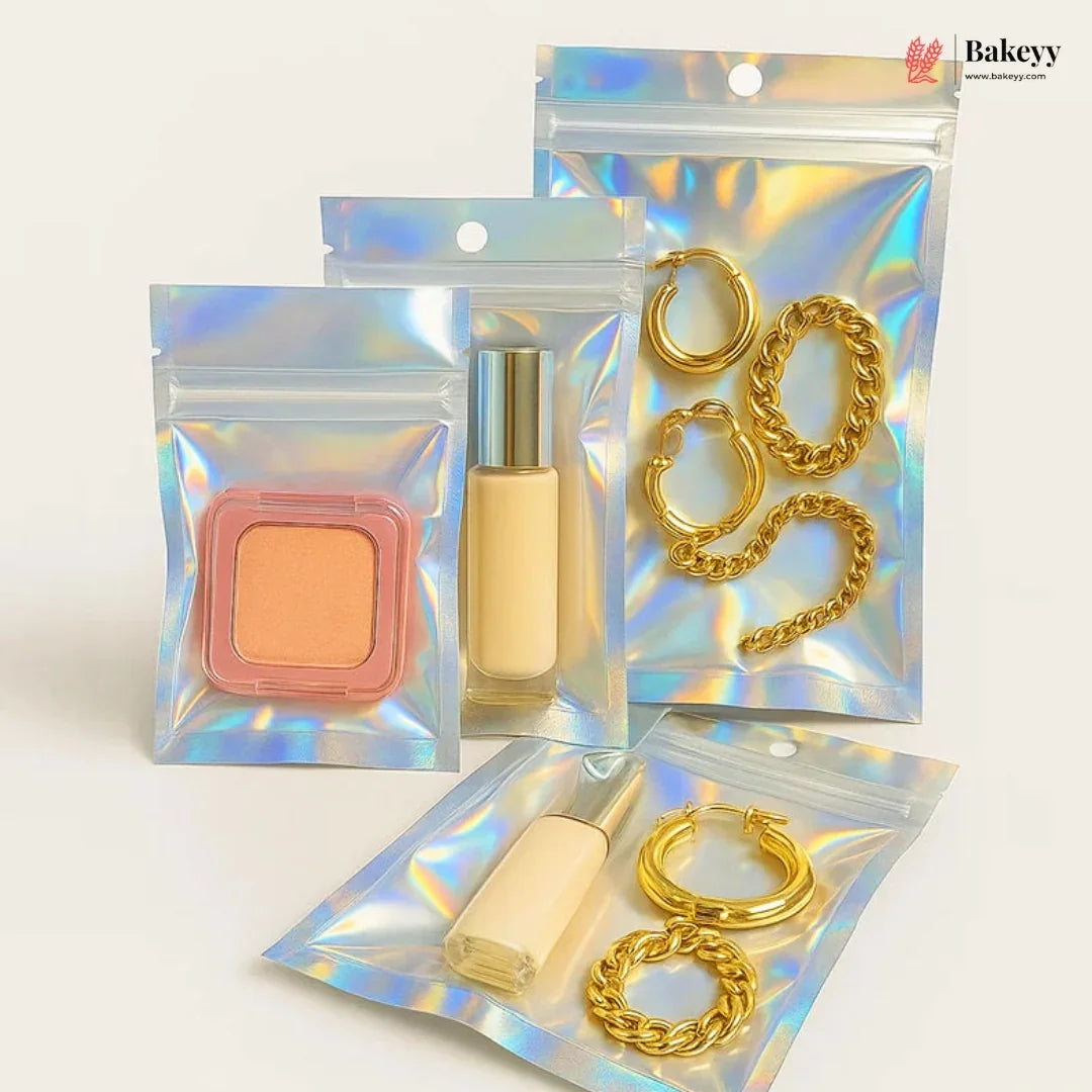 Four iridescent holographic zipper pouches arranged on a light beige background. Two pouches contain gold-tone chain and hoop earrings, and two contain cosmetic items: a peach-colored square compact and a beige liquid bottle with a silver cap.