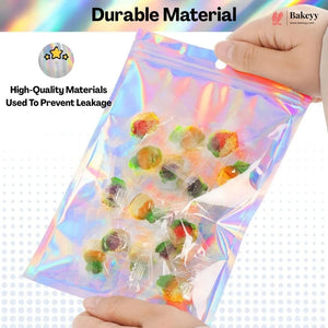 A hand holds a transparent holographic zip-top bag filled with assorted colorful gummy candies. The image includes marketing text reading 'Durable Material' and 'High-Quality Materials Used To Prevent Leakage,' with a Bakeey logo in the top right.