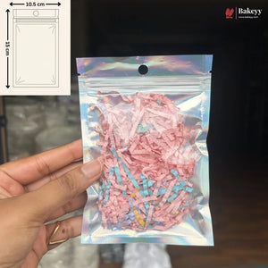 A hand holds a holographic silver resealable pouch filled with pink and blue shredded paper filler. The top-left corner shows a size diagram indicating 10.