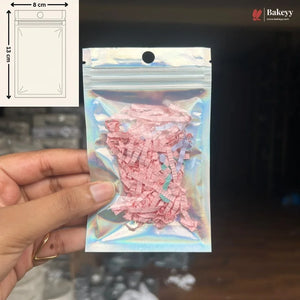 A hand holds a small holographic zipper pouch containing pink shredded paper filler. The pouch has a die-cut hanging hole at the top.