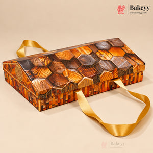 A rectangular wooden box with a honeycomb pattern of wood slices in various shades of brown, featuring a gold satin ribbon handle, set against a solid beige background. The Bakeyy brand logo is visible in the top right corner.