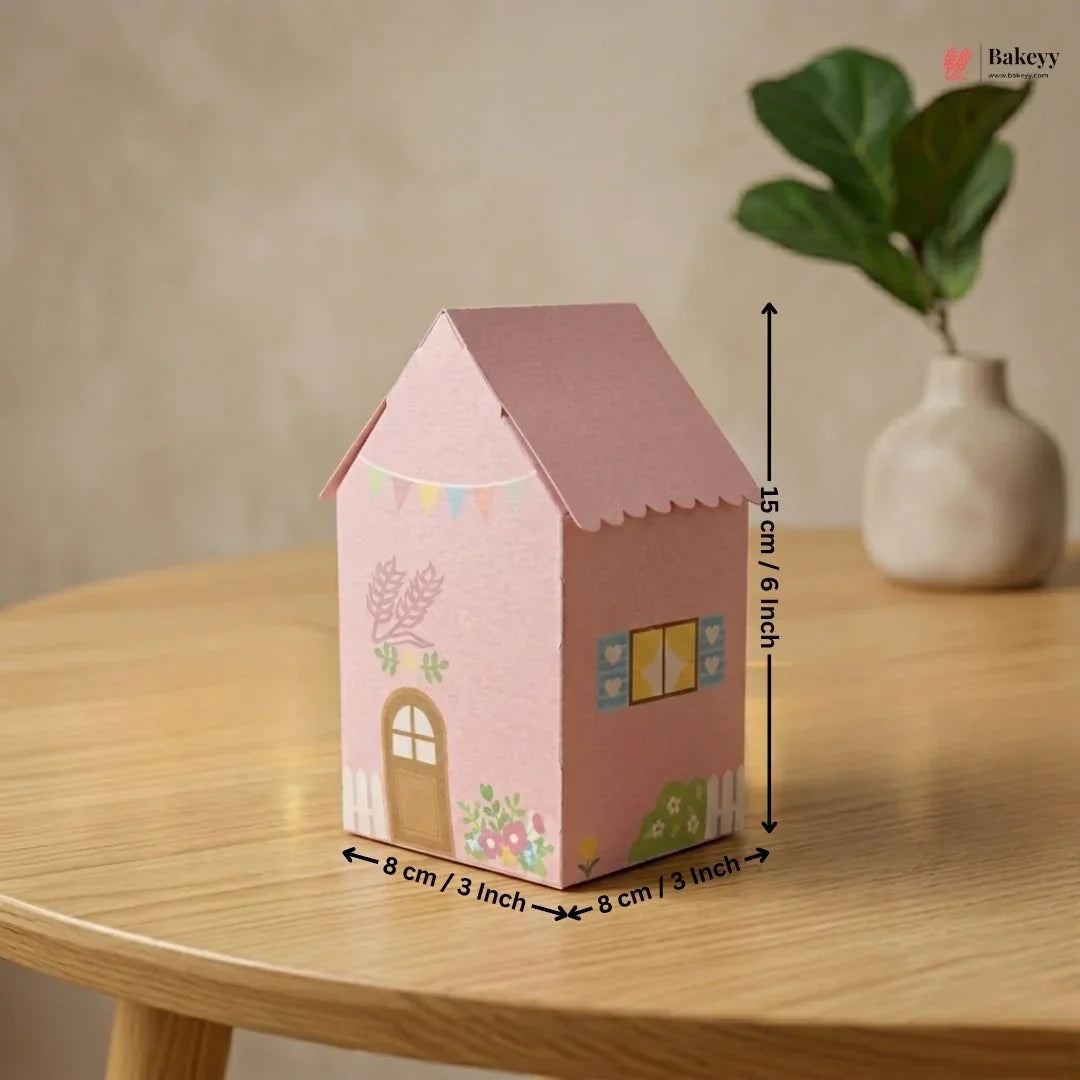 Pink house-shaped box with measurements on a wooden table, featuring a plant in the background.