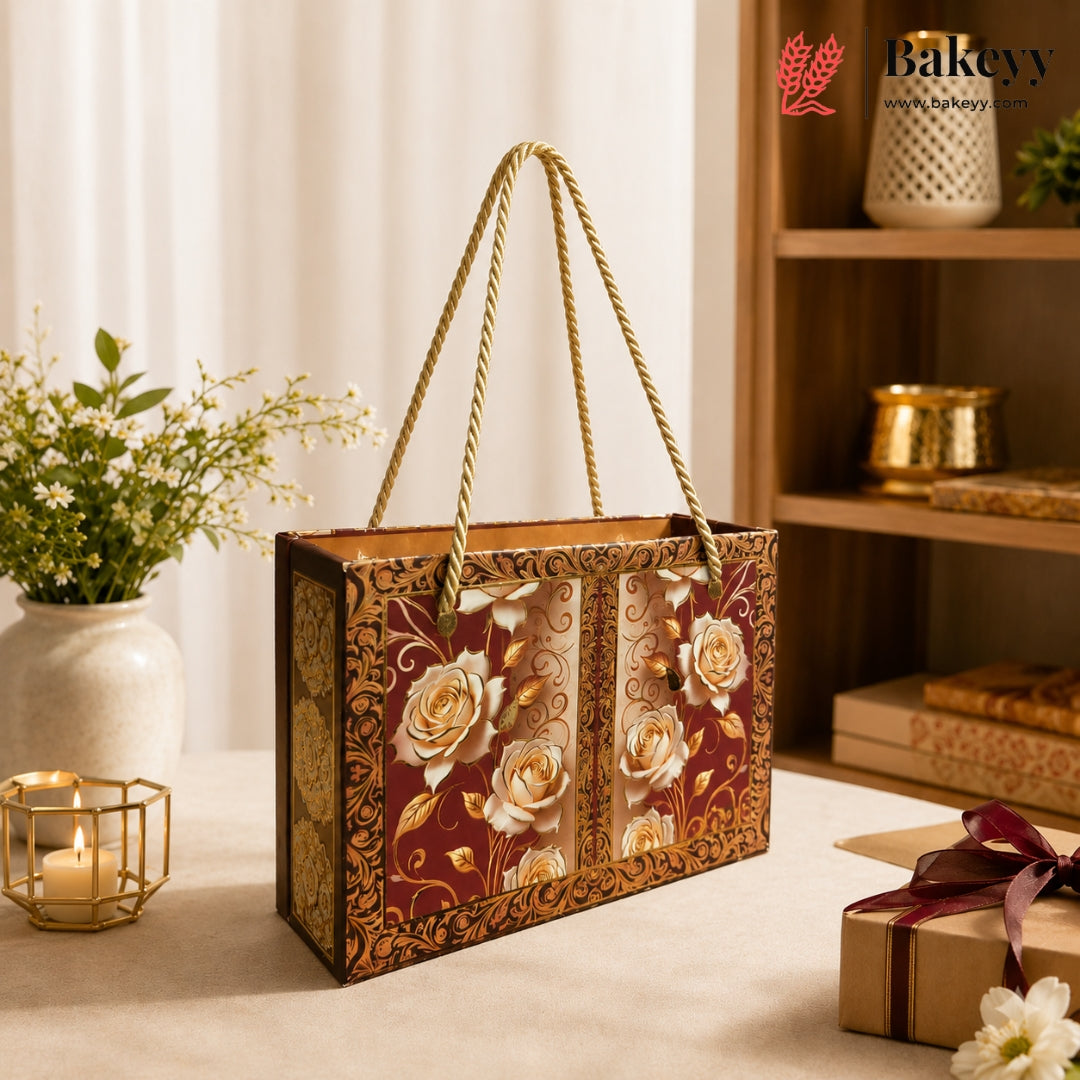 A decorative gift box with rope handles, featuring a burgundy and gold floral pattern with cream roses, displayed on a table in a warm, styled interior setting.