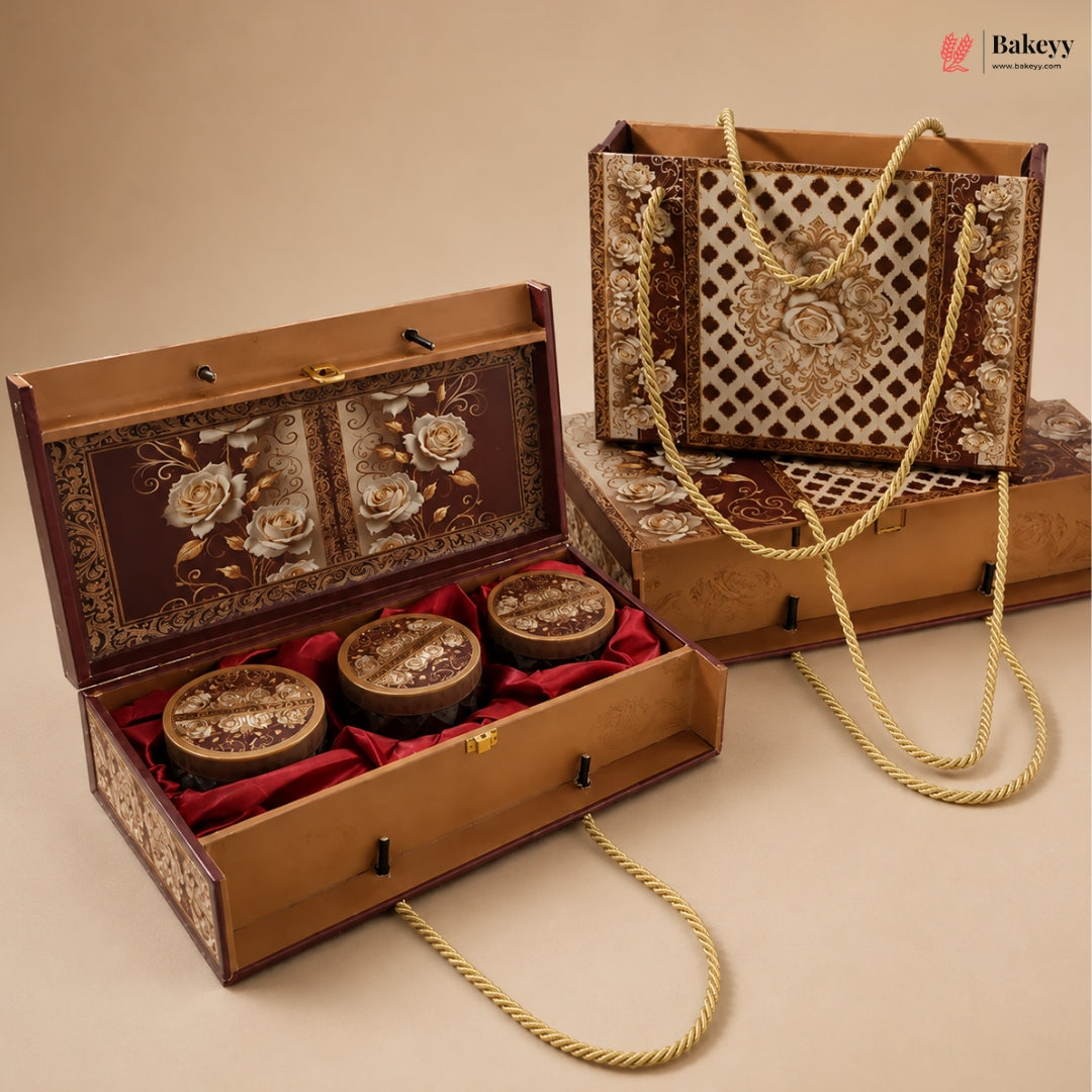 An ornate rectangular gift box set with a hinged wooden box shown open, containing three round decorative jars on red velvet lining, alongside a matching tote bag with rope handles and a closed box. The packaging features gold floral and geometric patterns on a dark brown background, photographed on a beige studio backdrop.