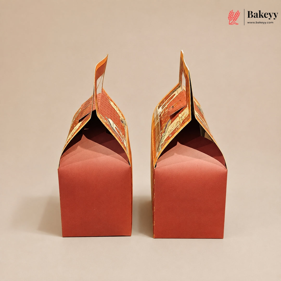 Two red paper gift boxes with orange printed handles, shown from the back on a plain beige background. A Bakeyy logo is visible in the top right corner.