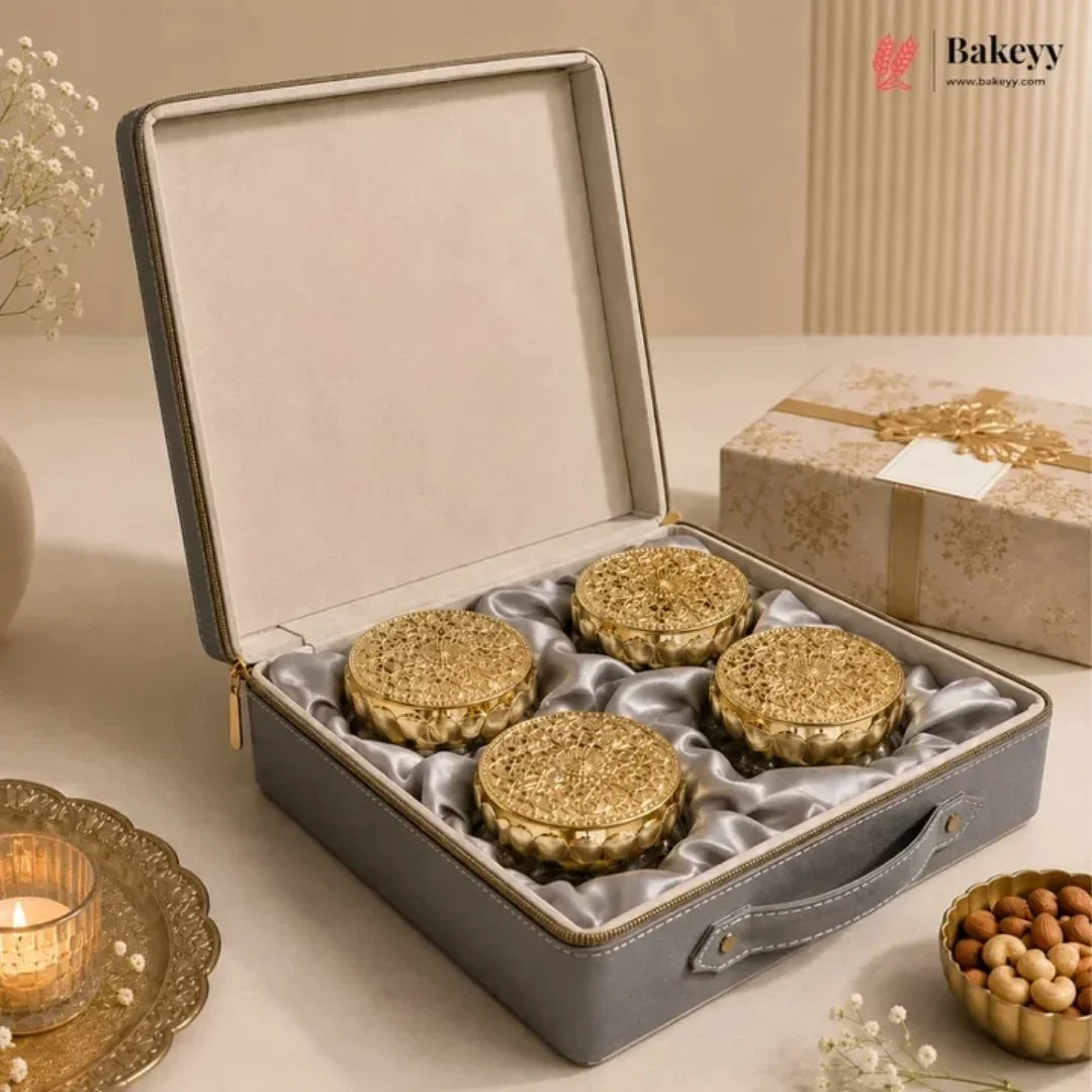 An open gray presentation box with a satin-lined interior holding four round golden-brown pastries, styled on a beige surface with decorative props and a branded Bakeyy logo in the top right.