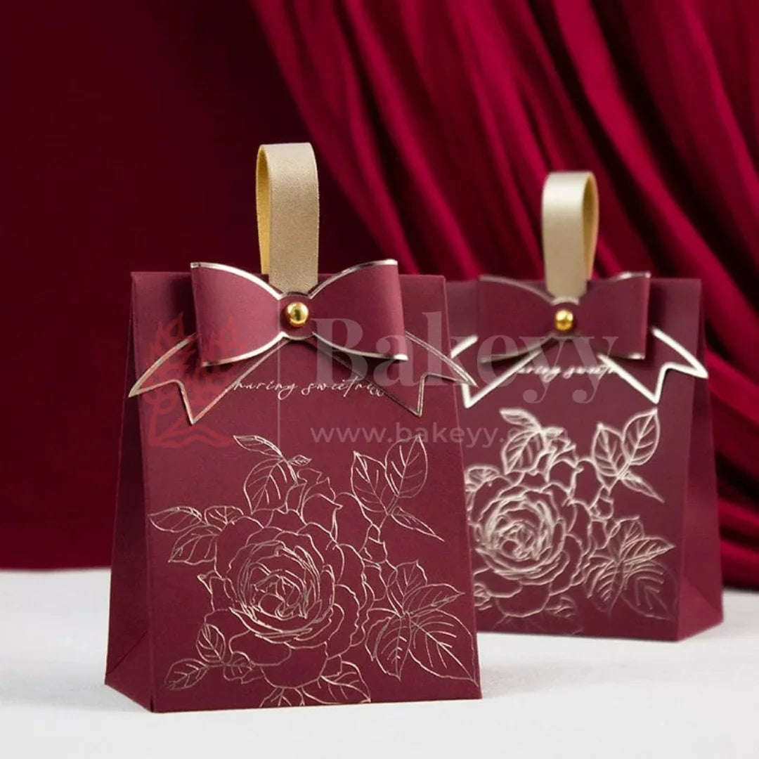 Two maroon gift bags with floral designs and gold ribbons on a red curtain background.