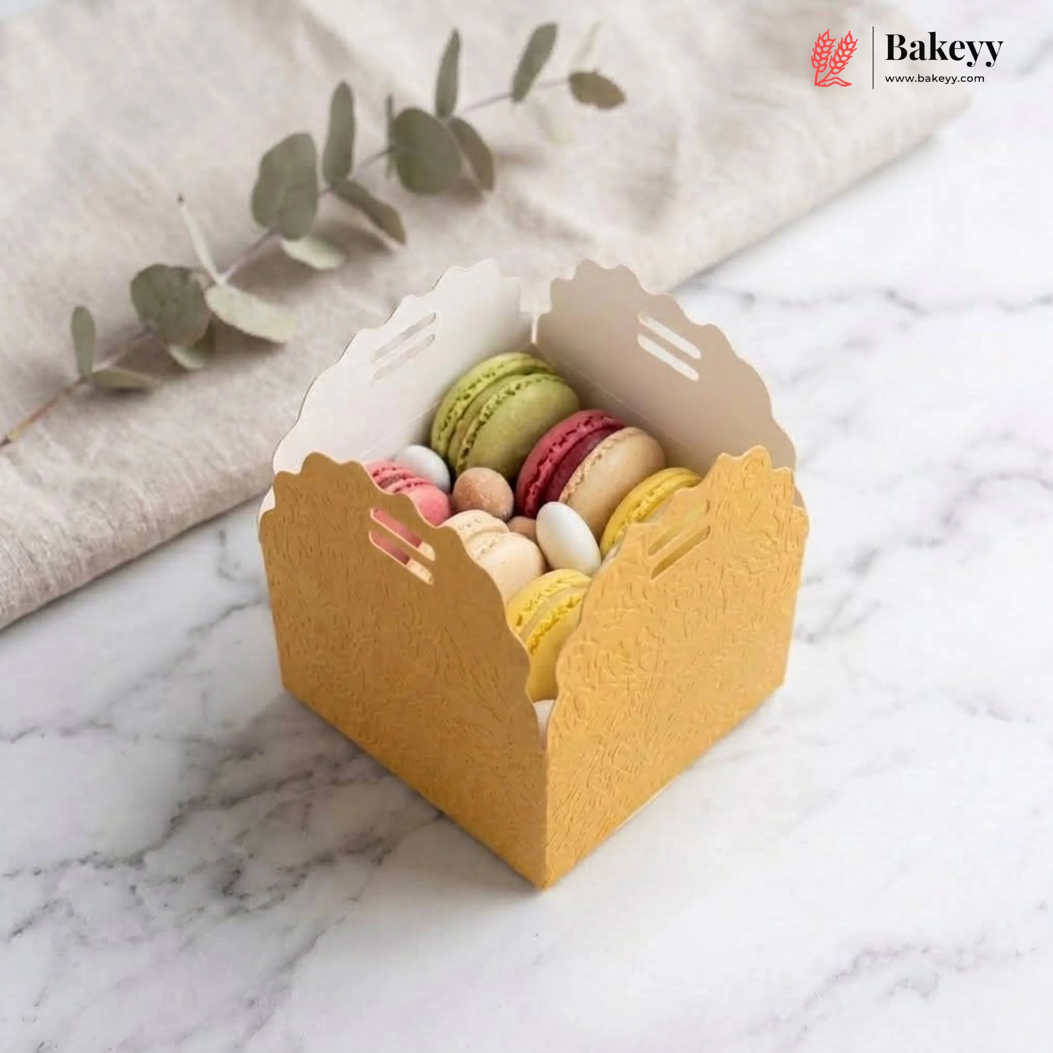 Small yellow box with colorful macarons on a marble surface, featuring the Bakeyy brand.