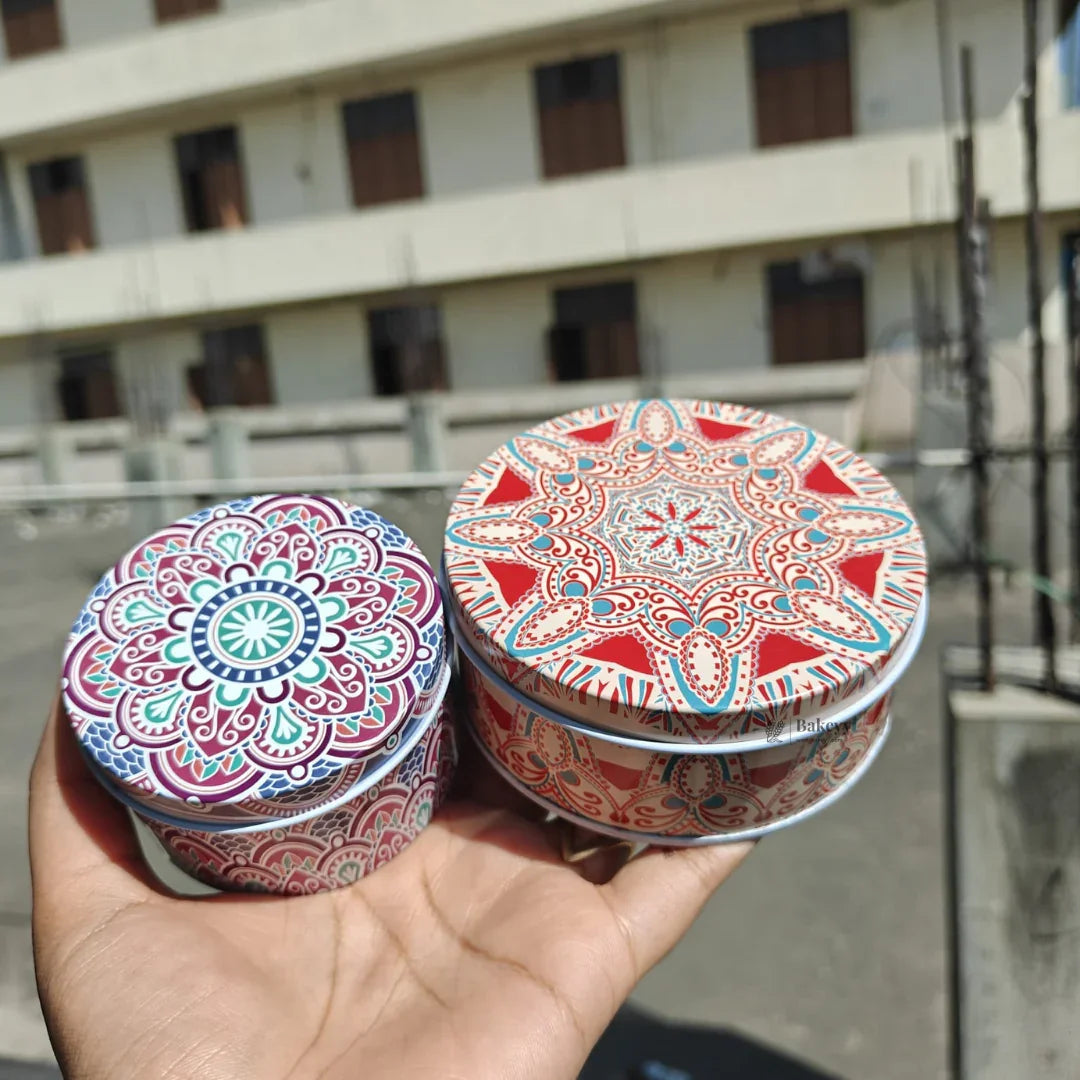 Hand holding two round tin boxes with colorful mandala prints, ideal for gift packaging from Bakeyy.com