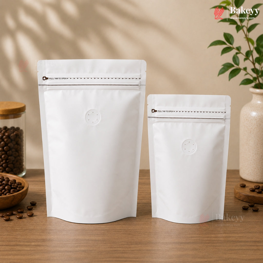 Two white stand-up resealable coffee bags of different sizes on a wooden table, with coffee beans and decorative props in the background.