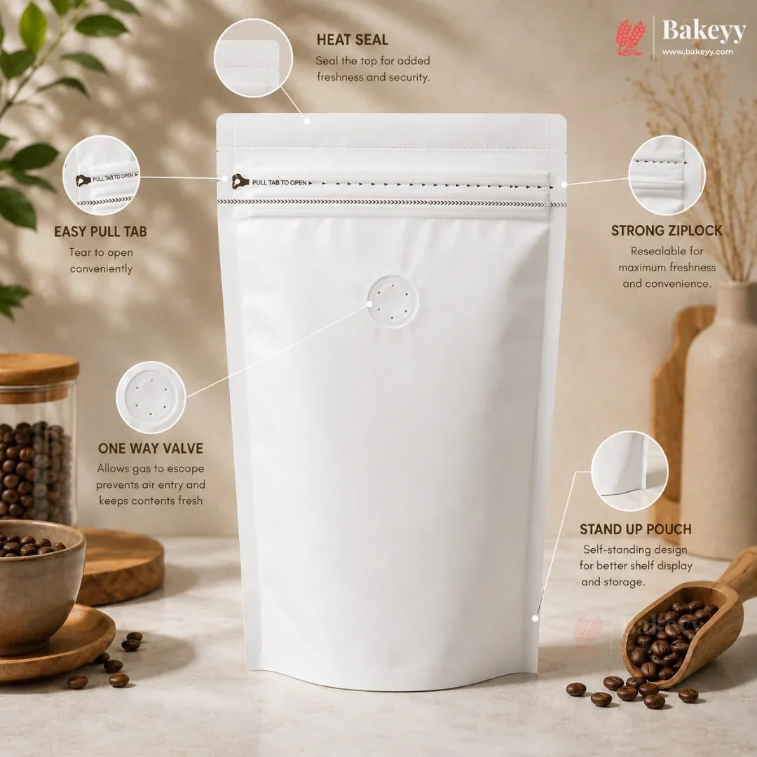 A white stand-up pouch packaging bag with a heat seal and one-way valve, shown with callout graphics and text explaining its features. The background is a warm, styled kitchen or cafe setting with coffee beans, a jar, and a wooden scoop.