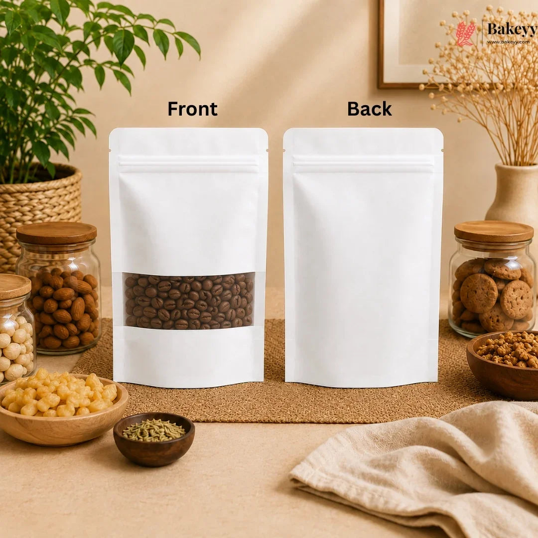 Two white stand-up resealable pouches labeled Front and Back, shown on a beige tabletop with food props and jars. The front pouch has a clear window revealing coffee beans, and the back is plain white.