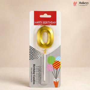 A gold metallic letter 'O' birthday candle in its retail blister packaging, featuring a red 'HAPPY BIRTHDAY' header and balloon graphics on a beige background.