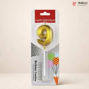 A gold metallic number 9 birthday candle in its original retail packaging, featuring a red 'HAPPY BIRTHDAY' header and festive balloon graphics on a beige background.