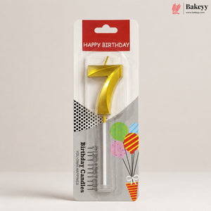 A gold metal number 7 birthday candle in its retail blister packaging, featuring a red 'HAPPY BIRTHDAY' header and festive balloon graphics on a neutral light gray background.
