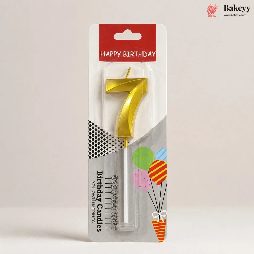 A gold metal number 7 birthday candle in its retail blister packaging, featuring a red 'HAPPY BIRTHDAY' header and festive balloon graphics on a neutral light gray background.