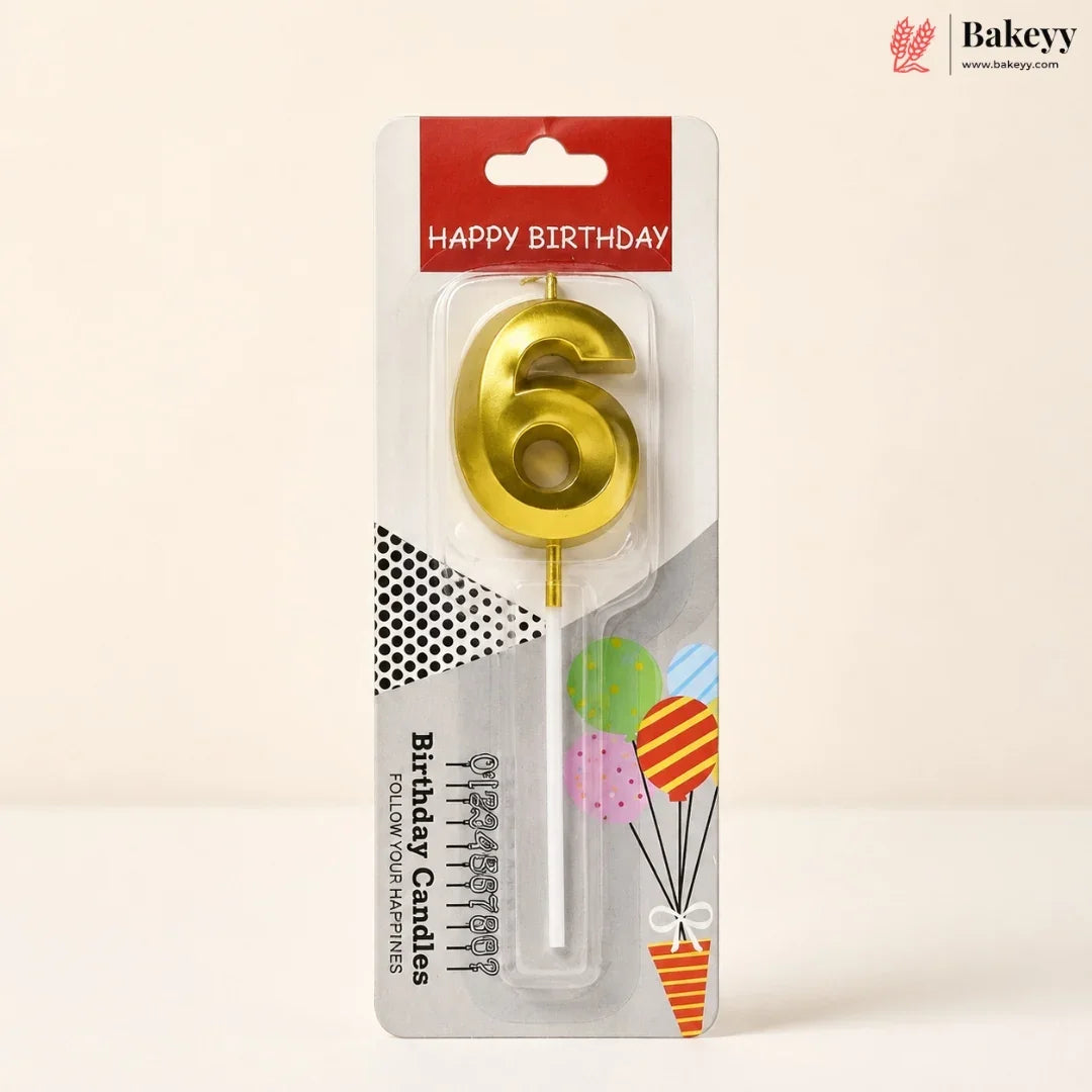 A gold metallic number 6 birthday candle in its original retail packaging, featuring a red 'HAPPY BIRTHDAY' header and festive balloon graphics on a light beige background.