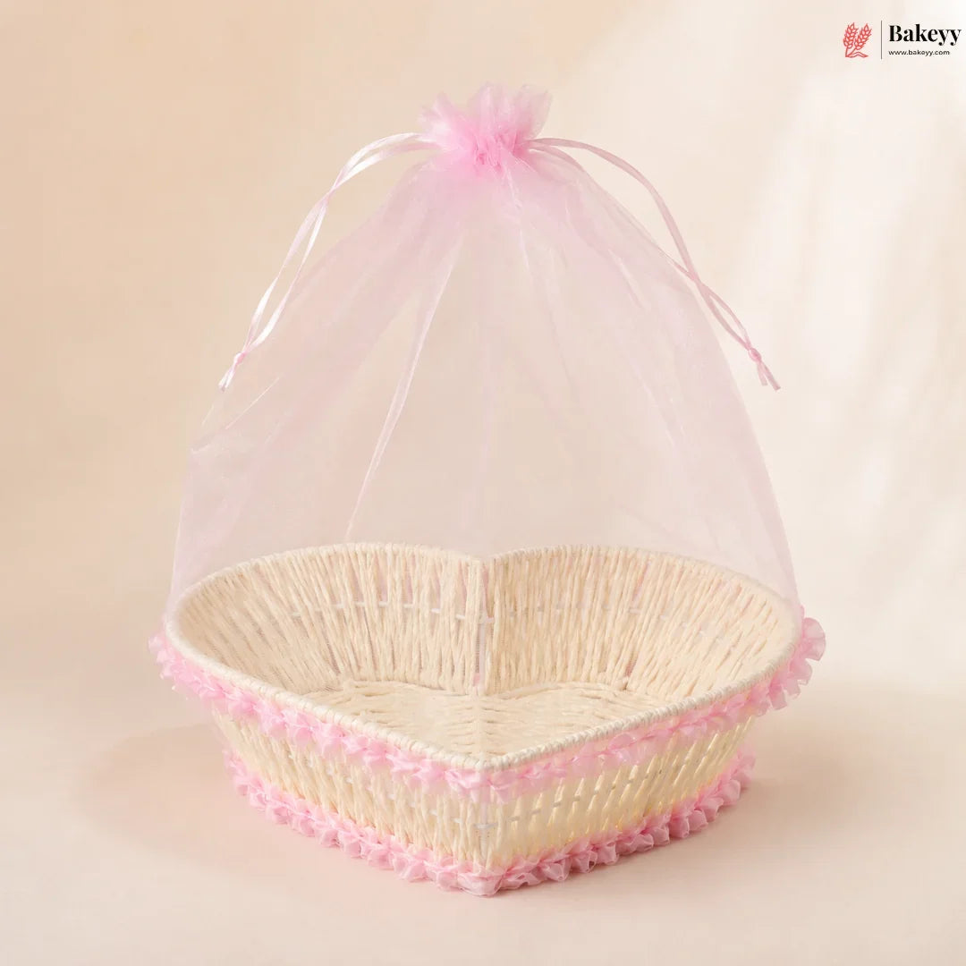 Heart-shaped wicker basket with pink decorative trim and sheer cover on a beige background, featuring the Bakeyy brand.