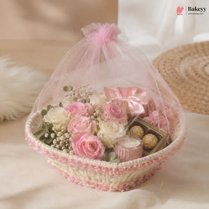 Decorative basket with pink roses, candles, and chocolates on a soft surface.