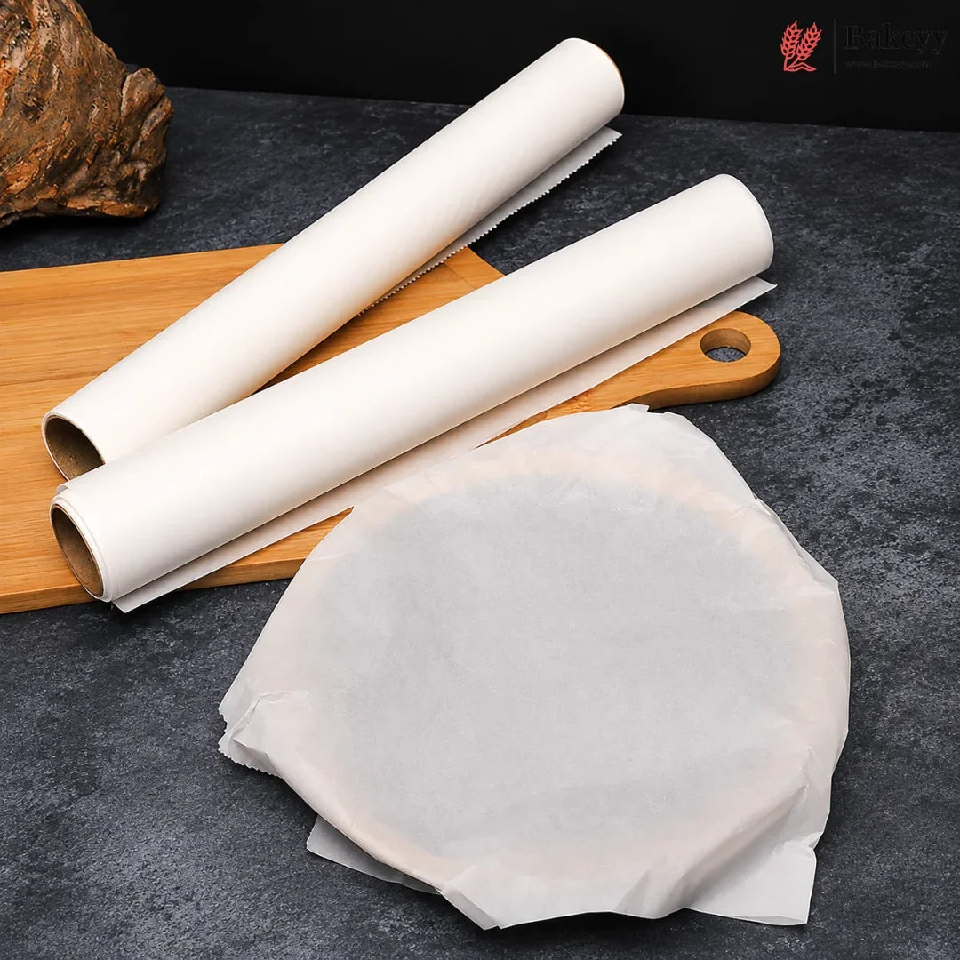 Two rolls of white parchment paper and a stack of unrolled sheets on a dark textured surface with a wooden cutting board prop.