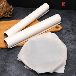 Two rolls of white parchment paper and a stack of unrolled sheets on a dark textured surface with a wooden cutting board prop.