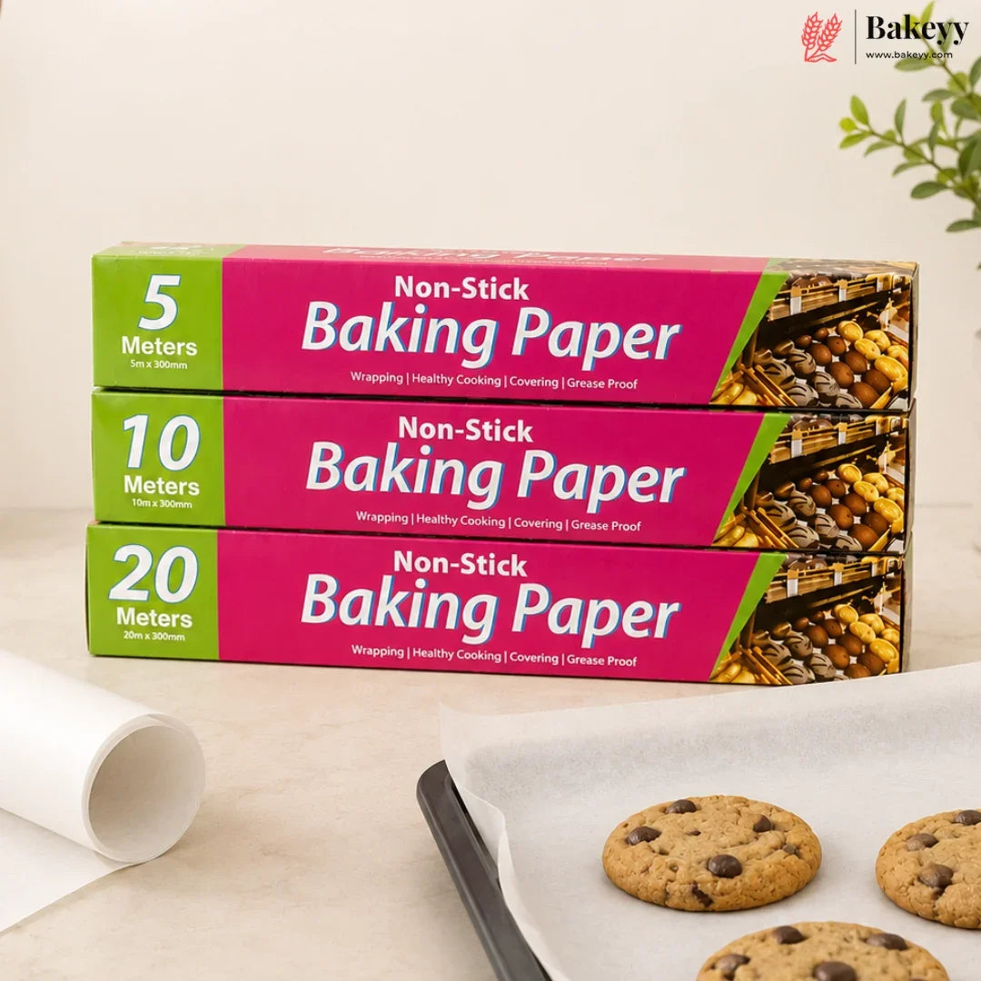Three boxes of non-stick baking paper in different quantities (5 meters, 10 meters, and 20 meters) stacked on a light beige surface next to a partially unrolled white sheet and a baking tray with chocolate chip cookies. The Bakey brand logo is visible in the top right corner.
