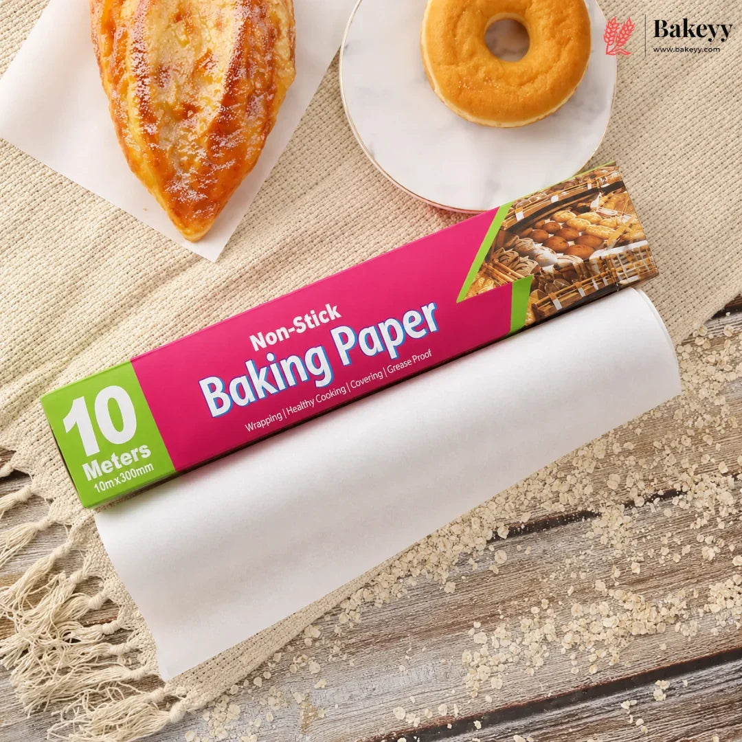 A roll of non-stick baking paper with a bright pink and green label, shown partially unrolled on a rustic burlap surface with baked goods and flour scattered around. The label reads '10 Meters Non-Stick Baking Paper'.