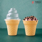 Two yellow waffle-cone-shaped dessert cups on a teal surface against a teal background. The left cup has a clear plastic tiered lid, and the right cup is filled with pink ice cream or gelato topped with chocolate drizzle and sprinkles.