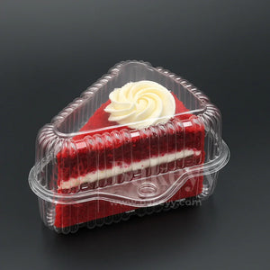 Slice of red velvet cake with white frosting in a clear plastic container on a black background