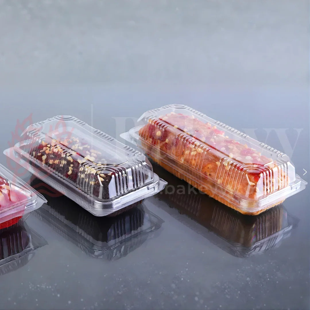 Three cake slices in clear plastic containers on a reflective surface with a blurred background.