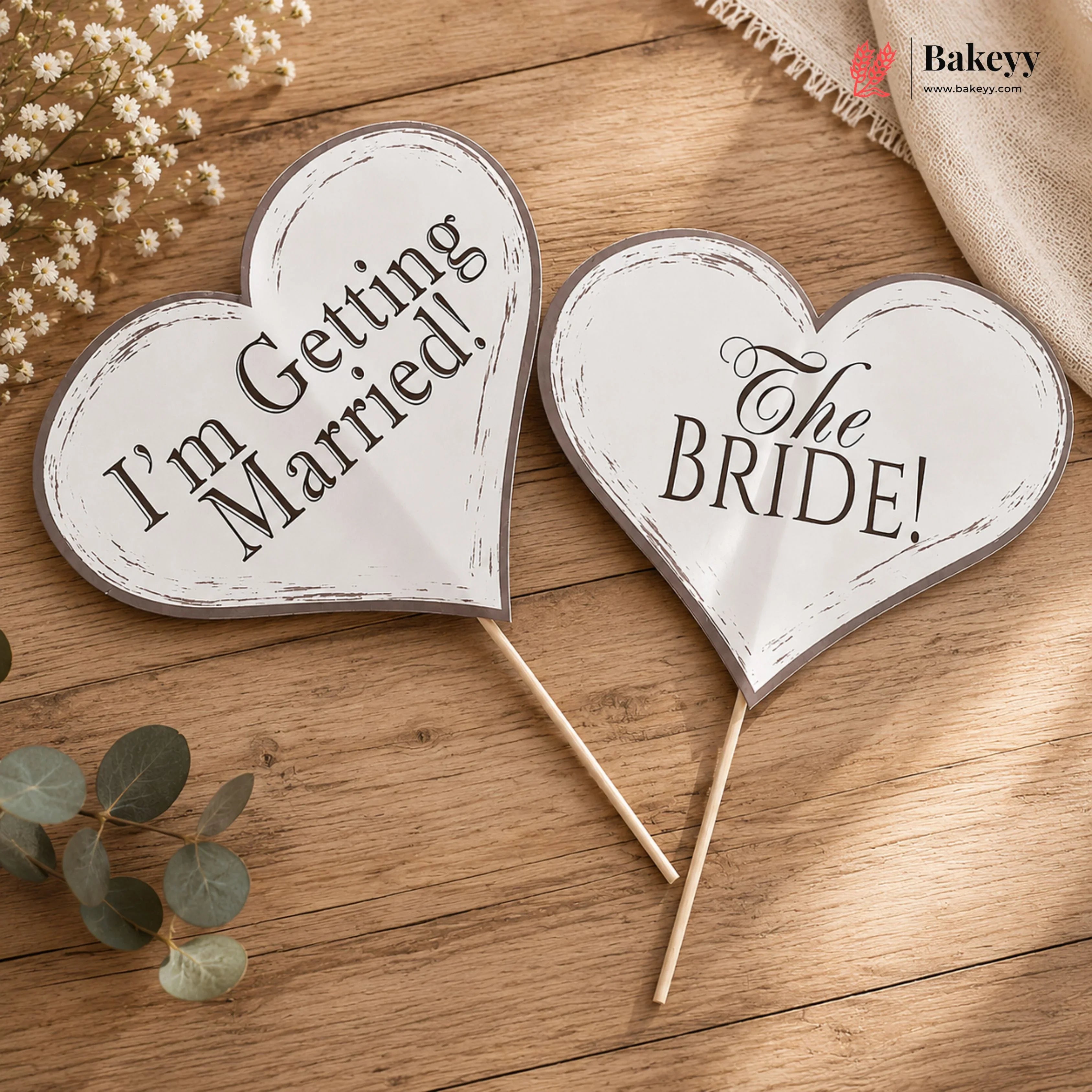 Heart-shaped signs on sticks with 'I'm Getting Married!' and 'The BRIDE!' text on a wooden surface.