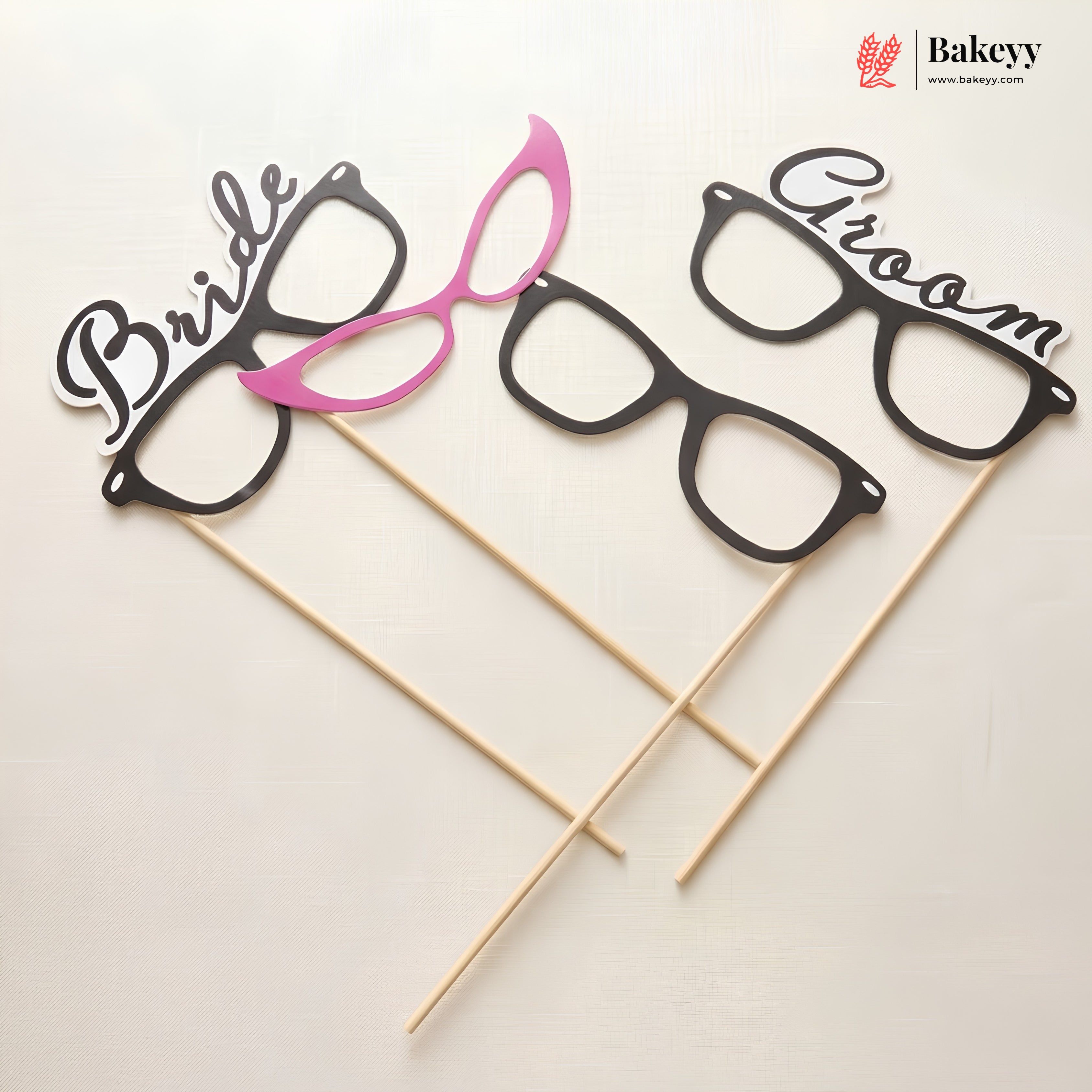 Glasses-shaped photo booth props labeled 'Bride' and 'Groom' on sticks with Bakeyy branding.