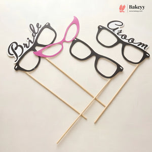 Glasses-shaped photo booth props labeled 'Bride' and 'Groom' on sticks with Bakeyy branding.