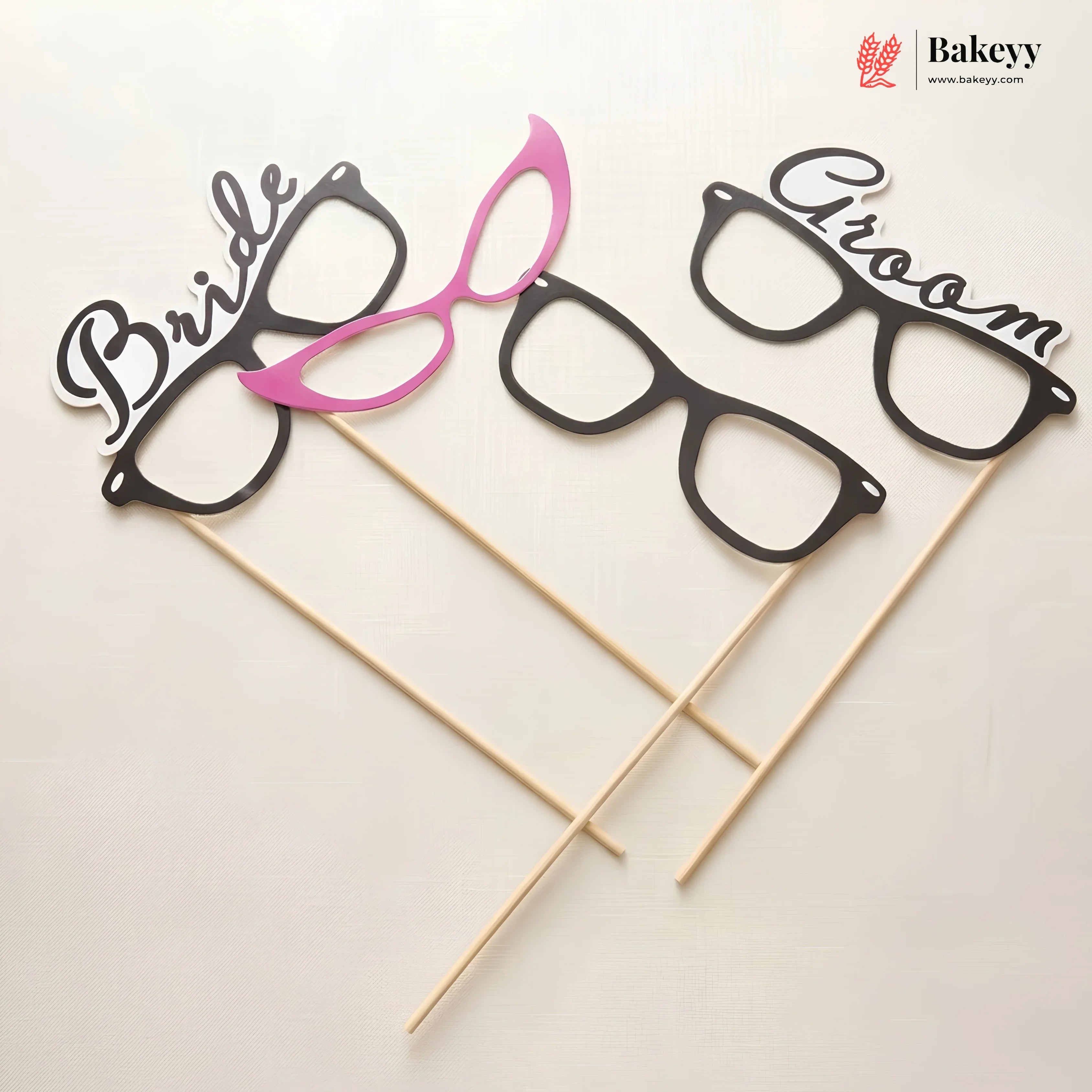 Glasses-shaped photo booth props labeled 'Bride' and 'Groom' on sticks with Bakeyy branding.