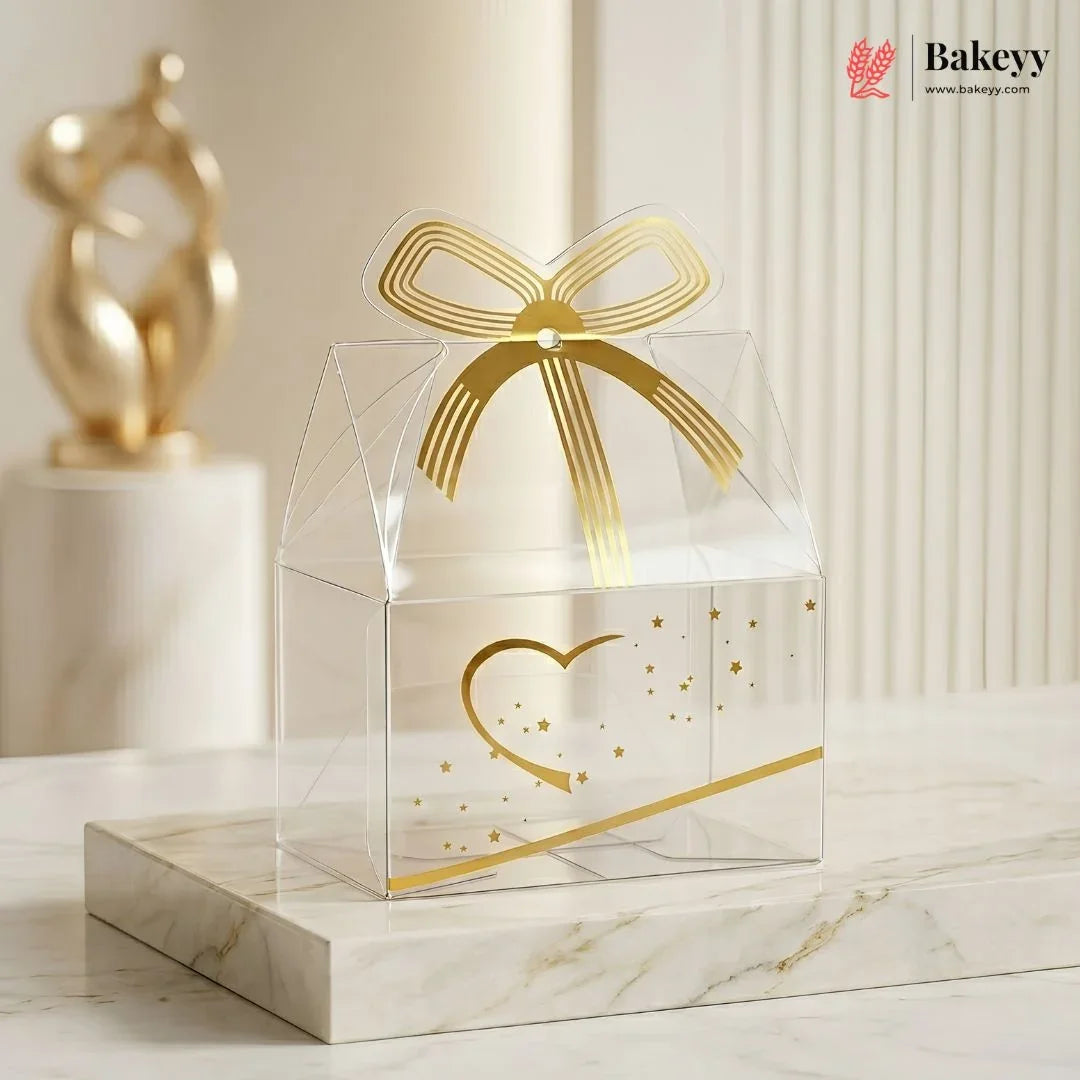 Clear gift box with gold bow and heart design on a marble surface, featuring the Bakey brand.
