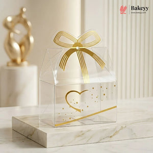 Clear gift box with gold bow and heart design on a marble surface, featuring the Bakey brand.