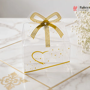 Clear gift box with gold bow and heart design on a marble surface, featuring the brand 'Bakeys'.