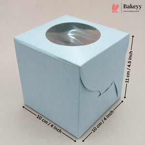 A light blue square paper gift box with a circular clear window on top, shown with dimension arrows and labels indicating 10 cm by 10 cm by 11 cm measurements. The Bakeyy logo appears in the top right corner.
