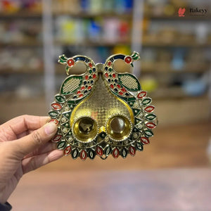 Decorative gold diya with peacock design held by a hand against a blurred background